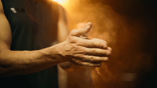 Cropped view of blurred sportsman applying talc on hands on dark background