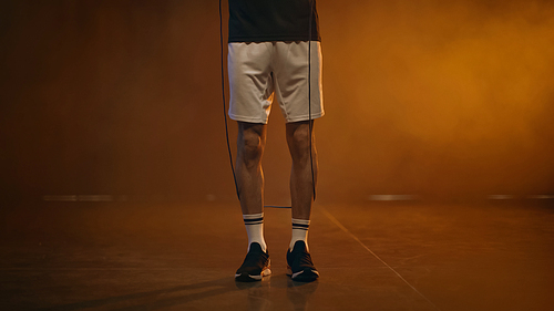 Cropped view of sportsman holding jump rope on dark background