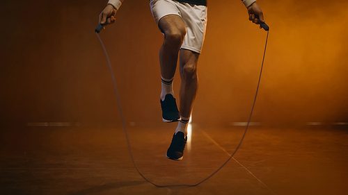 Cropped view of sportsman jumping with rope on dark background