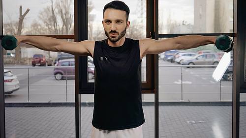 Bearded sportsman working out with dumbbells in gym