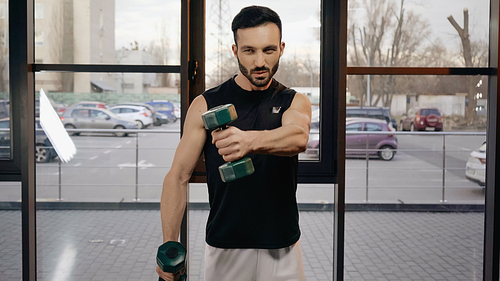 Muscular sportsman looking away while training with dumbbells in gym