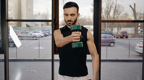 Muscular sportsman holding dumbbell while working out in gym