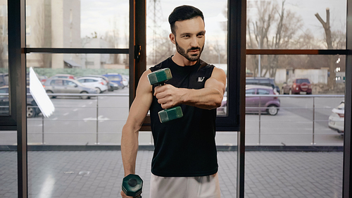 Sportsman in sportswear training with dumbbells in gym