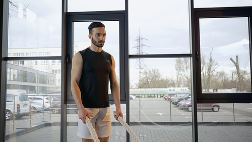 Athletic sportsman holding battle rope in gym