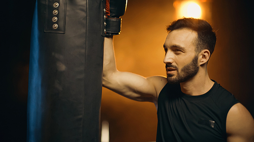 Boxer in glove looking at punch bag on dark background