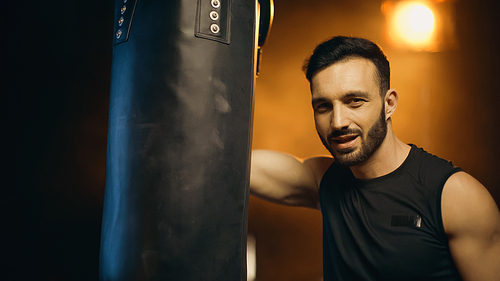 Smiling sportsman  near punch bag on dark background