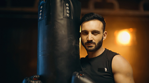 Bearded sportsman in gloves  near punch bag on dark background