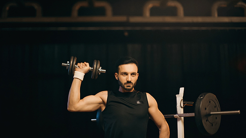 Brunette sportsman training with dumbbell on dark background