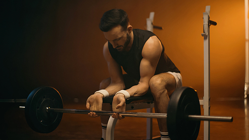 Muscular man training with barbell on flat bench on dark background