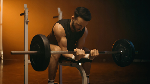 Athletic sportsman working out with barbell on dark background