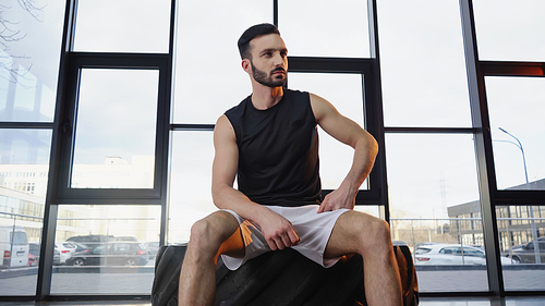 Bearded sportsman sitting on tire in gym