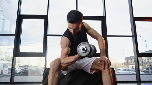 Fit sportsman training with dumbbell on tire in gym