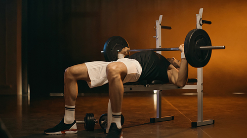 Athletic sportsman working out with barbell on dark background