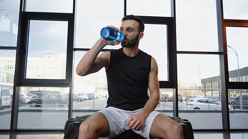 Sportsman drinking water while sitting on tire in gym