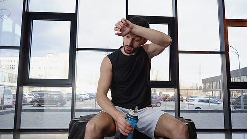 Tired sportsman holding sports bottle on tire in gym