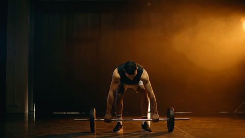 Muscular man training with barbell on dark background