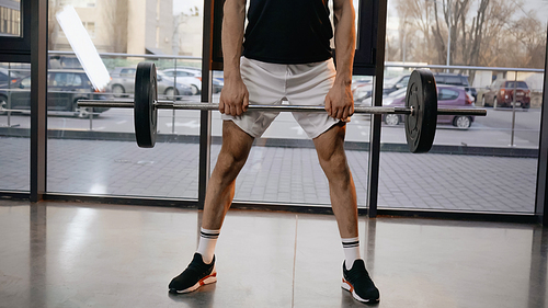 Cropped view of athletic sportsman holding barbell in sports center