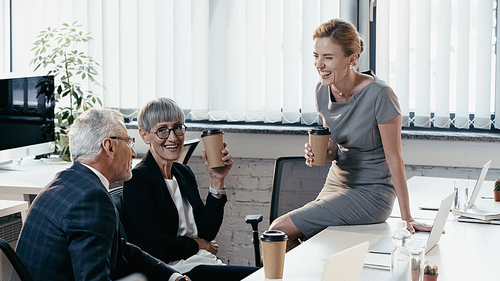 Happy business people holding paper cups while talking in office