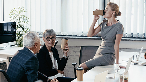 Business people with paper cups talking near devices in office