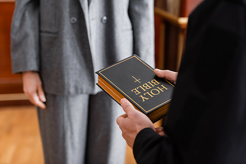 partial view of bailiff holding holy bible near woman in court