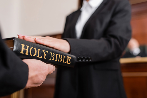 cropped view of blurred woman giving swear on bible during litigation