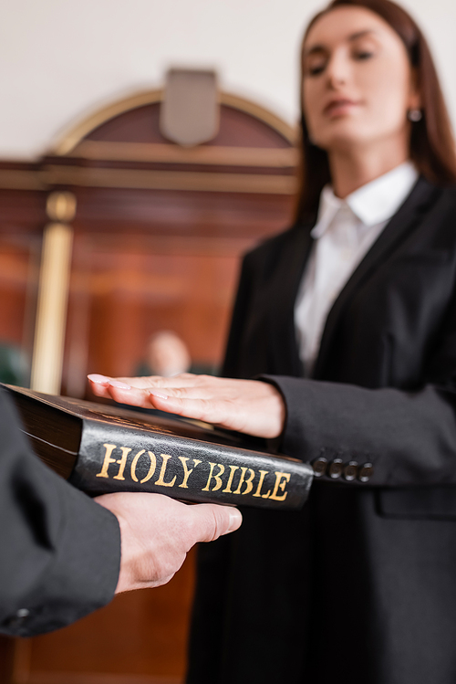 blurred woman giving oath on bible in hand of bailiff in courtroom