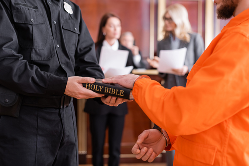 bailiff in uniform holding bible near accused man giving oath in court