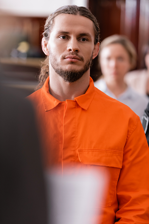 selective focus of bearded man in orange jail uniform standing in courtroom