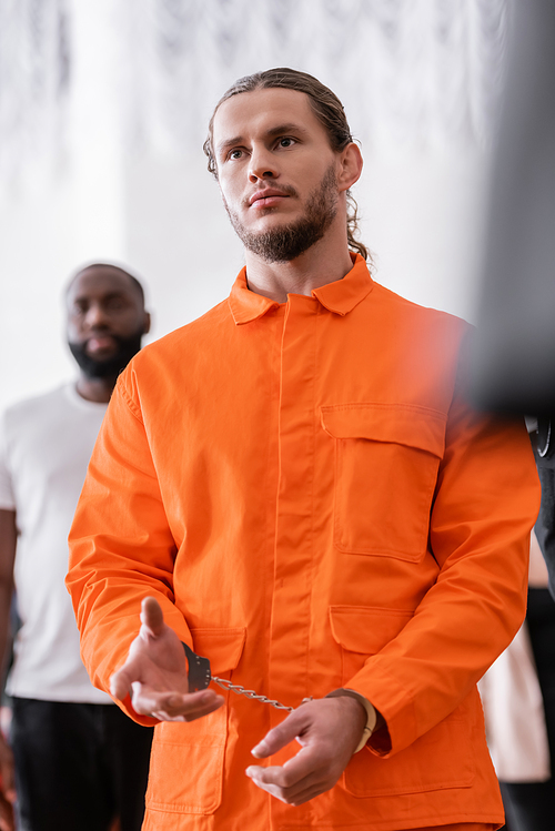 bearded man in handcuffs and orange jail uniform gesturing in courtroom