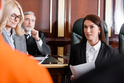 blonde advocate smiling near prosecutor and senior judge on background