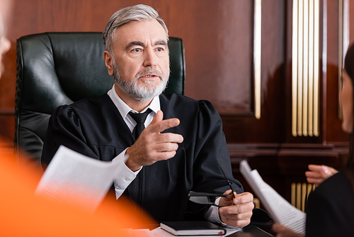 senior judge pointing with finger near blurred prosecutor with papers in court