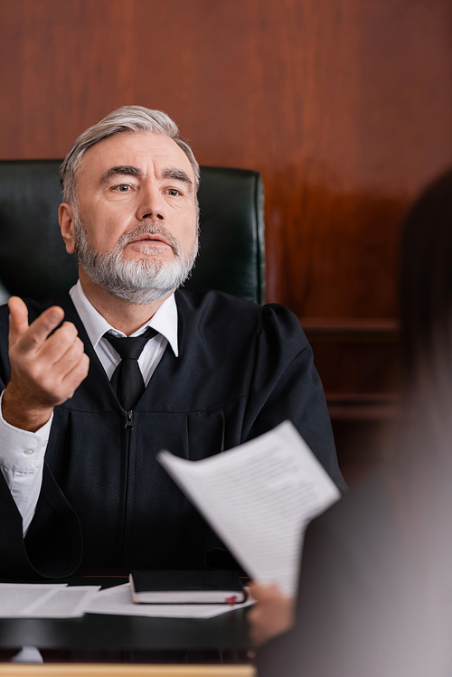 senior judge pointing with finger while talking to blurred prosecutor in courtroom