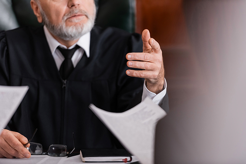 cropped view of judge pointing with finger at prosecutor with lawsuit on blurred foreground