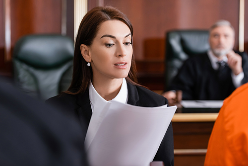 brunette prosecutor reading lawsuit in court on blurred foreground