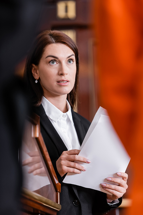 brunette lawyer holding documents in courtroom on blurred foreground