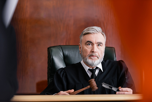 serious judge holding gavel and eyeglasses in court on blurred foreground