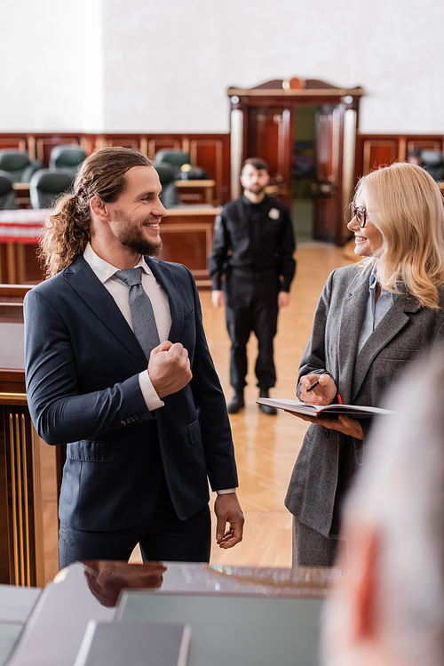 justified businessman showing success gesture near smiling advocate and blurred judge in court