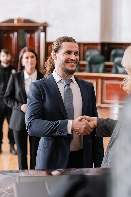 cheerful businessman shaking hands with blurred attorney in courtroom