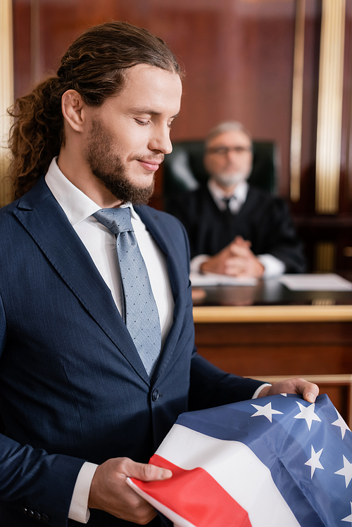 positive lawyer holding usa flag in courtroom near senior judge on blurred background