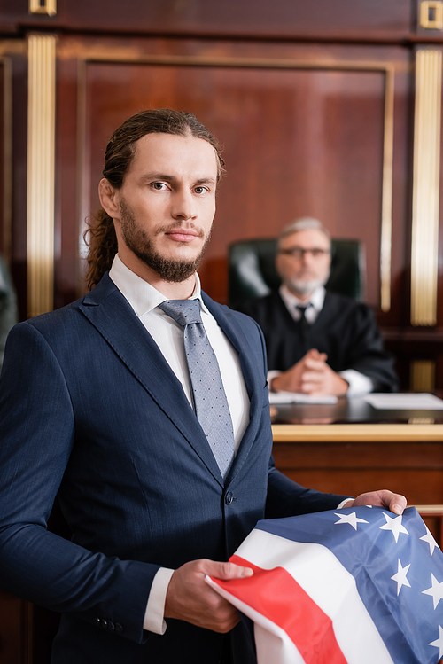 attorney  while holding usa flag near blurred judge in courtroom
