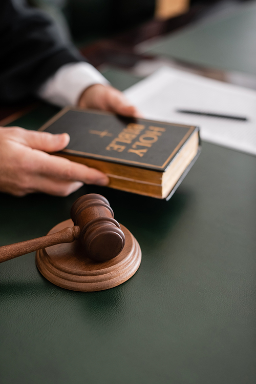 partial view of blurred judge holding bible near gavel in court