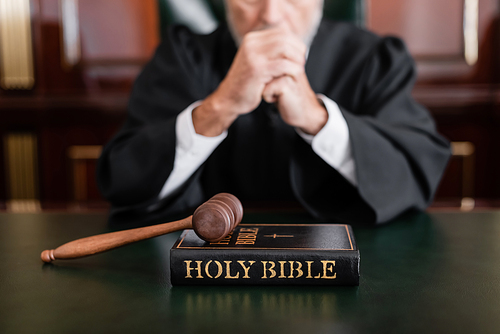 selective focus of bible and gavel near cropped judge on blurred background