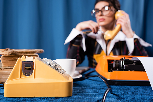 selective focus of vintage telephone near blurred newswoman talking on blue background