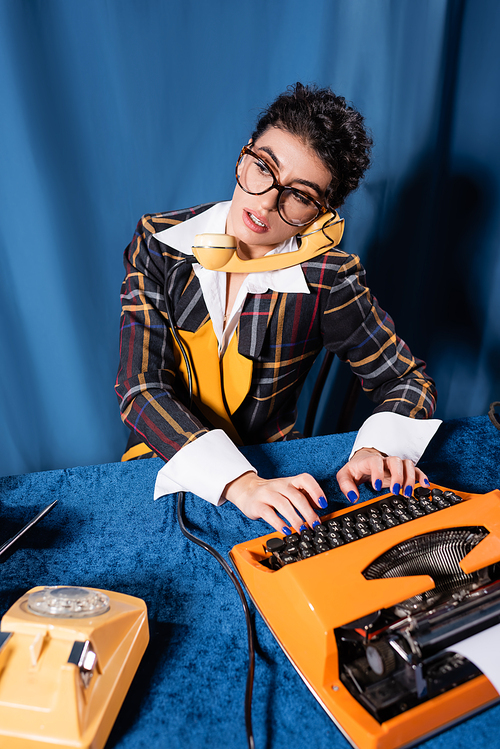 journalist in vintage style clothes calling on telephone while typing on blue background