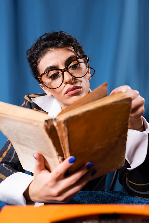 retro style newswoman in eyeglasses reading blurred book on blue background