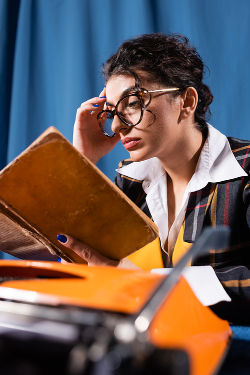 stylish woman in eyeglasses reading vintage book on blue background