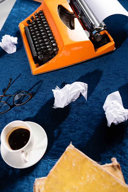 top view of coffee cup near vintage typewriter, eyeglasses and crumpled paper on blue velour tablecloth