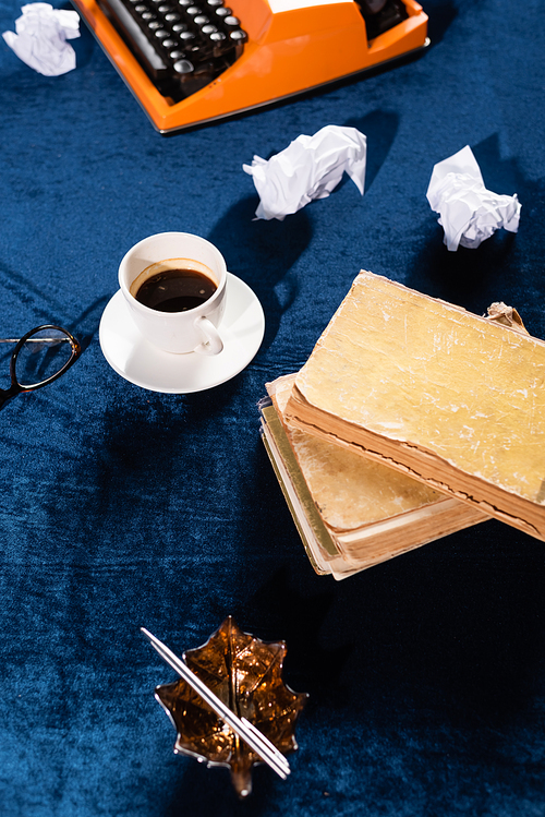 coffee cup, tattered books, crumpled paper and vintage typewriter on blue velour tablecloth