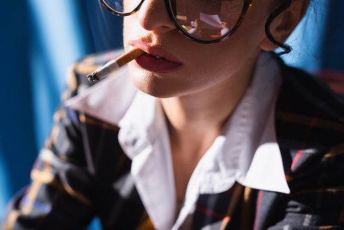 partial view of blurred vintage style woman smoking on blue background