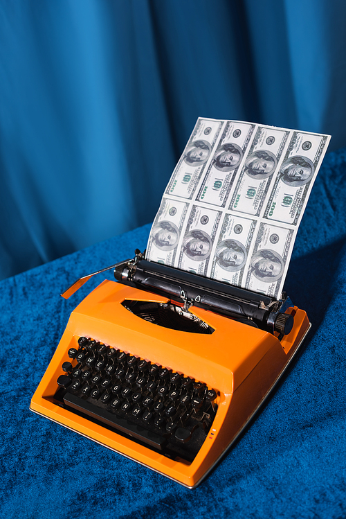 vintage typewriter and dollar banknotes on velour tablecloth and blue background